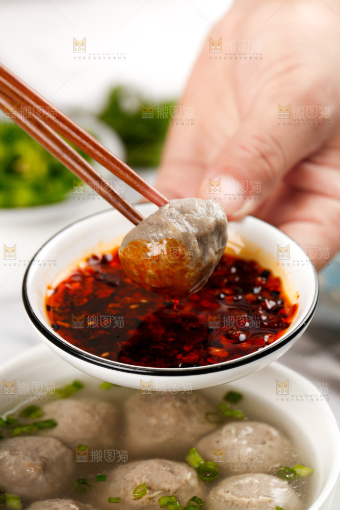 筷子夹着牛肉丸蘸辣椒