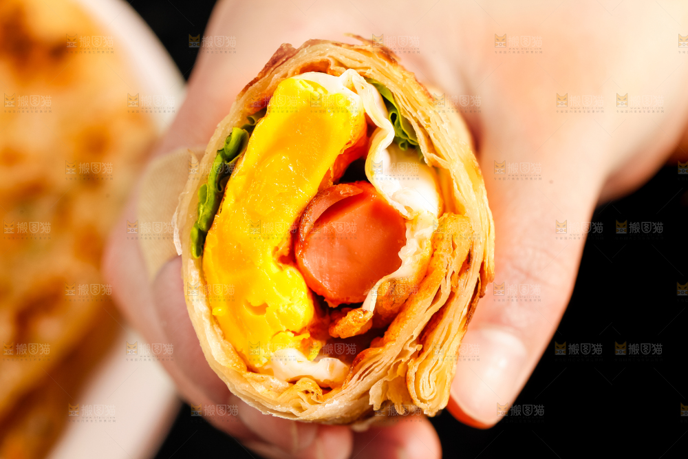 手拿着鸡蛋香肠卷饼